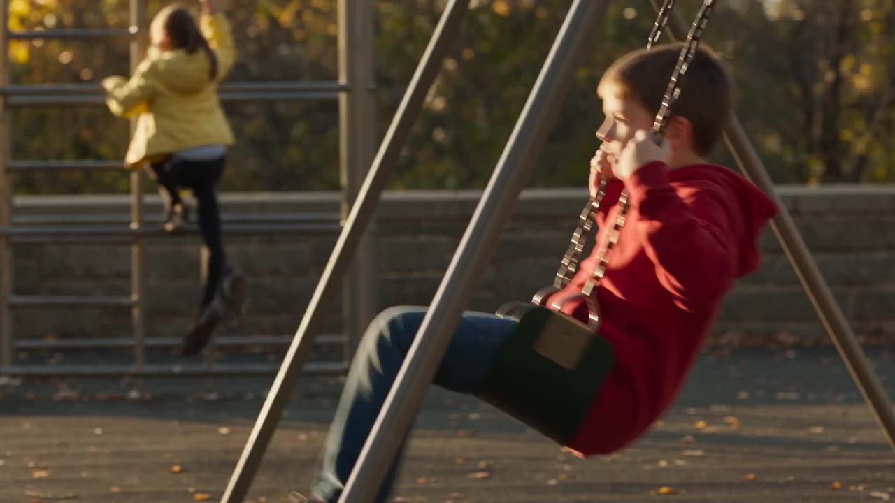 A public plaza and playground in late-afternoon light, with children playing and people sitting nearby.